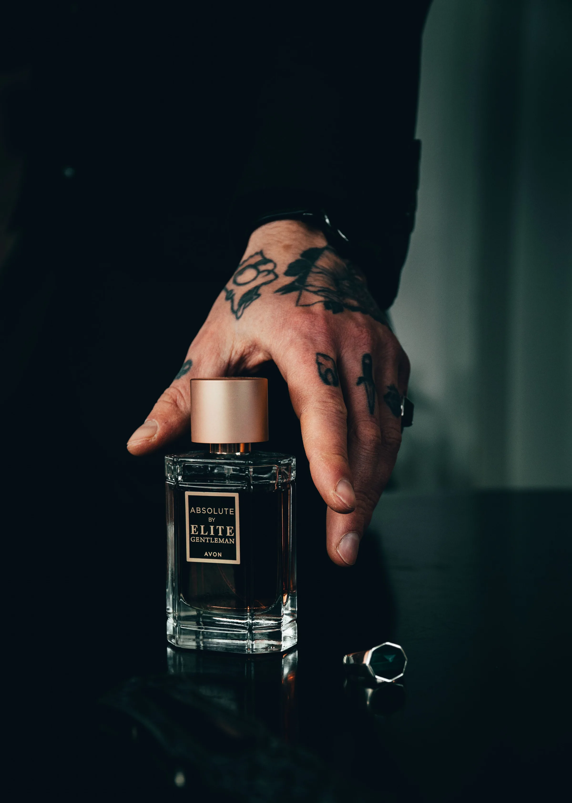 A hand holding a dark glass perfume bottle in low light